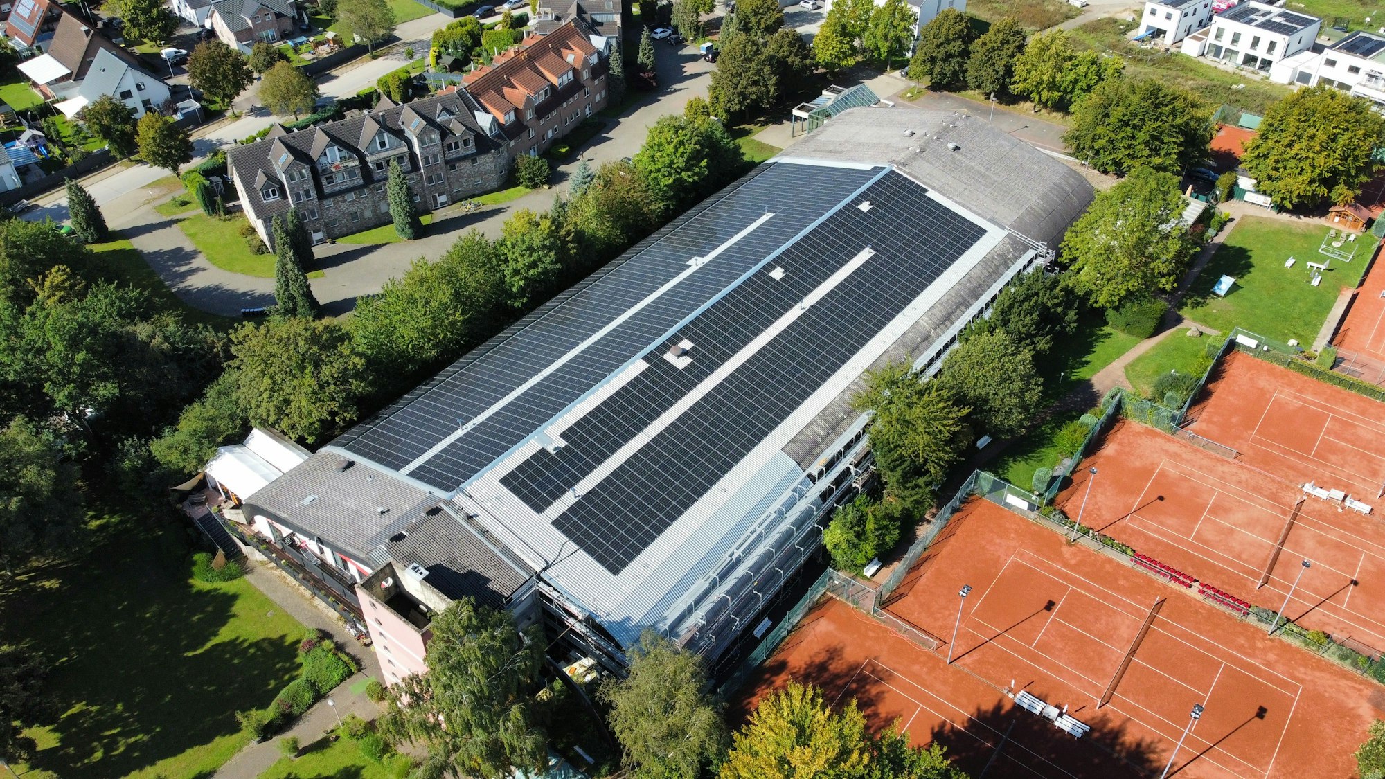 Das Foto zeigt eine großflächige Photovoltaikanlage auf einem Gebäude, angrenzend befinden sich mehrere Tennisplätze.