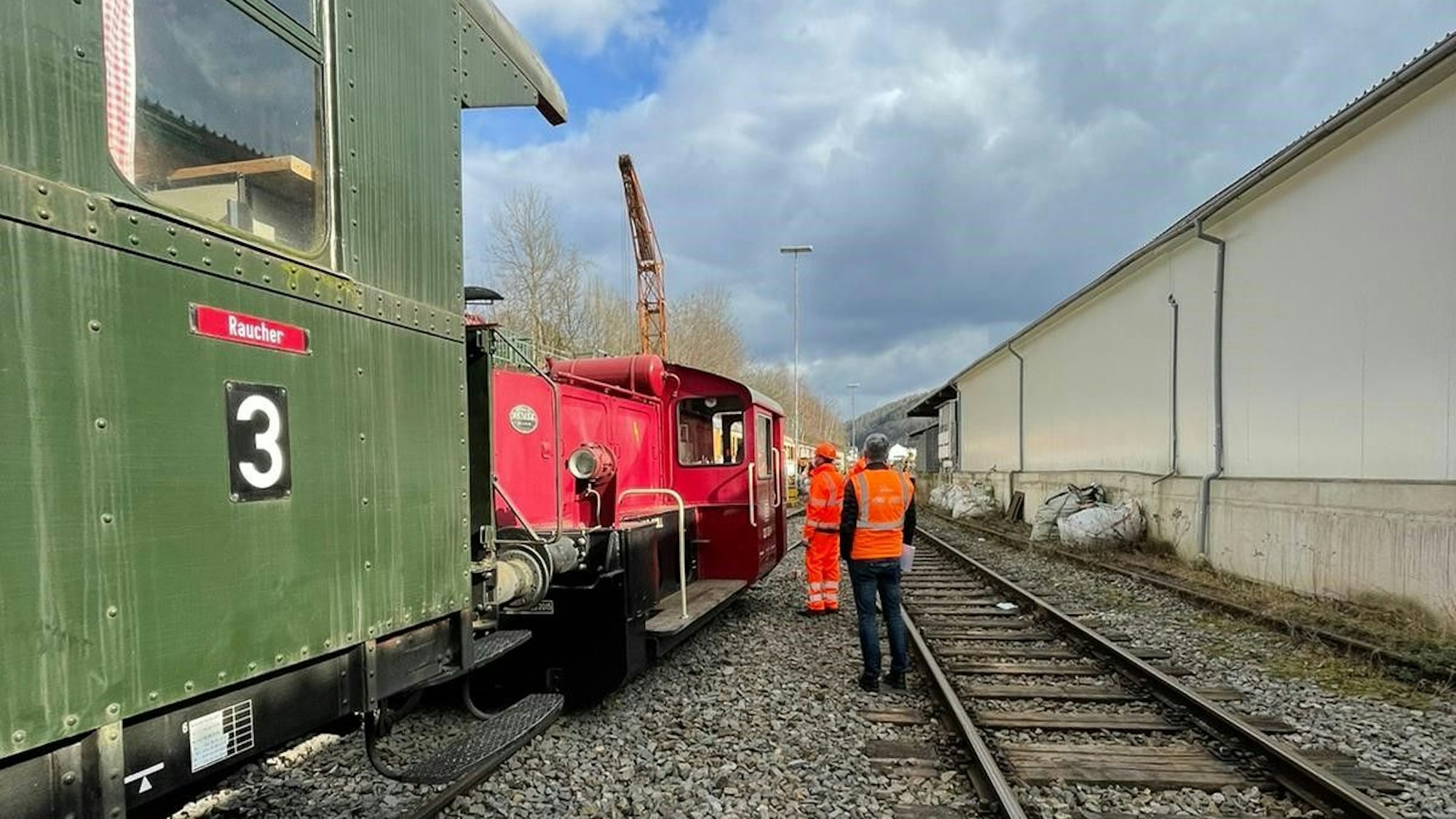 Lokführer-Aspiranten und Ausbilder stehen neben einer Rangierlok mit einem Waggon.
