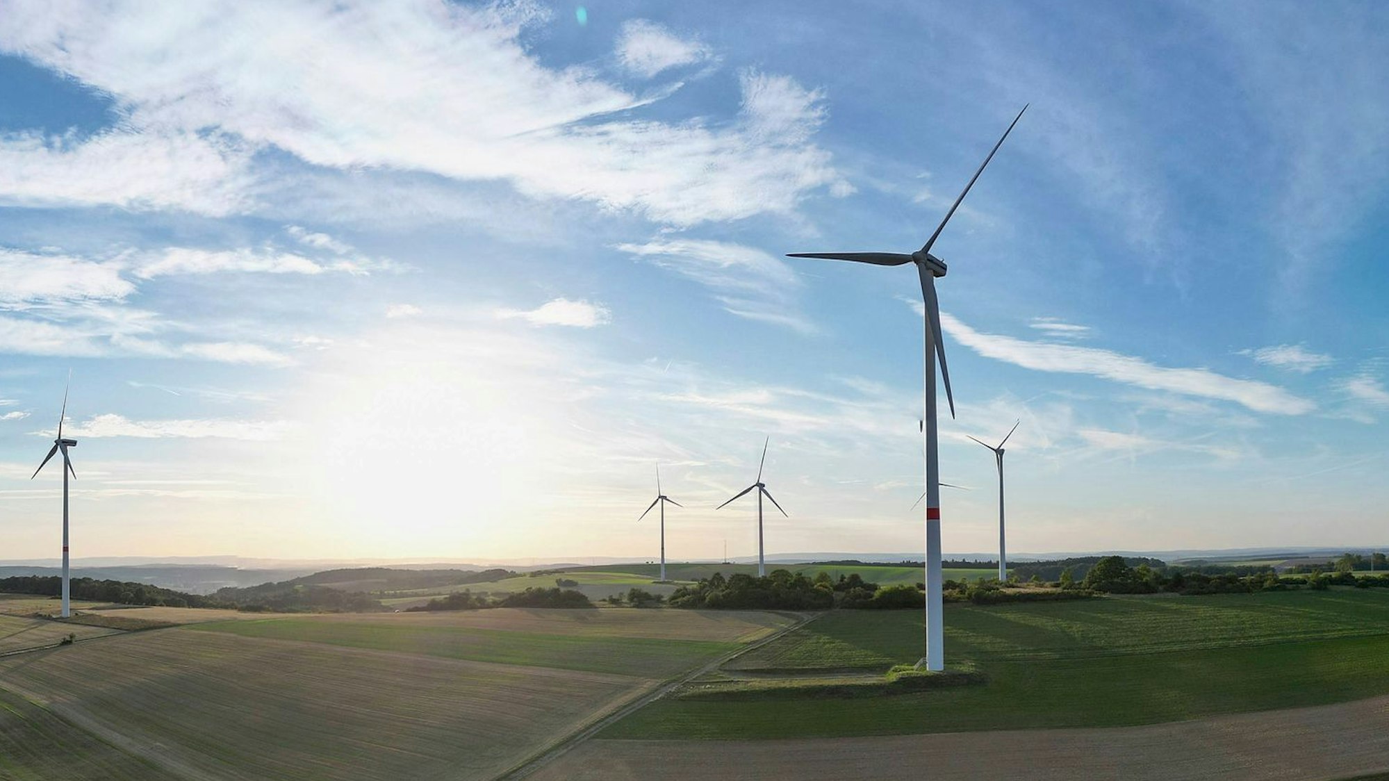 Windkraftanlagen stehen in einer Landschaft mit Feldern und Wäldern.