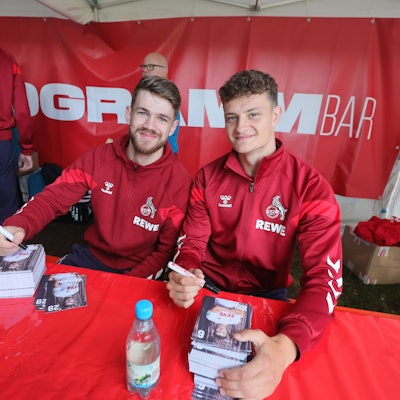 Jan Thielmann und Eric Martel sitzen an einem Tisch und unterschreiben Autogrammkarten.