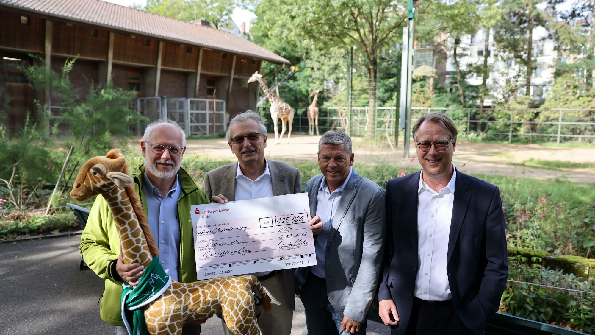 Theo Pagel, Dr. Löaus Tiedeken, Christopher Landsberg und Uwe Schönberg stehen mit einem Check vor dem Giraffengehege im Kölner Zoo.
