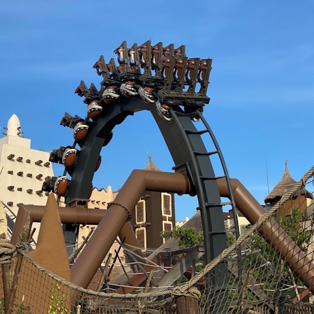 Die Achterbahn Black Mamba im Phantasialand fährt durch einen Looping. Im Hintergrund sieht man die Themenwelt „Deep in Africa“.