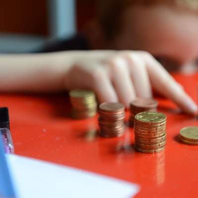 Ein fünfjähriger Junge sitzt an einem roten Tisch und zählt sein gespartes Taschengeld.