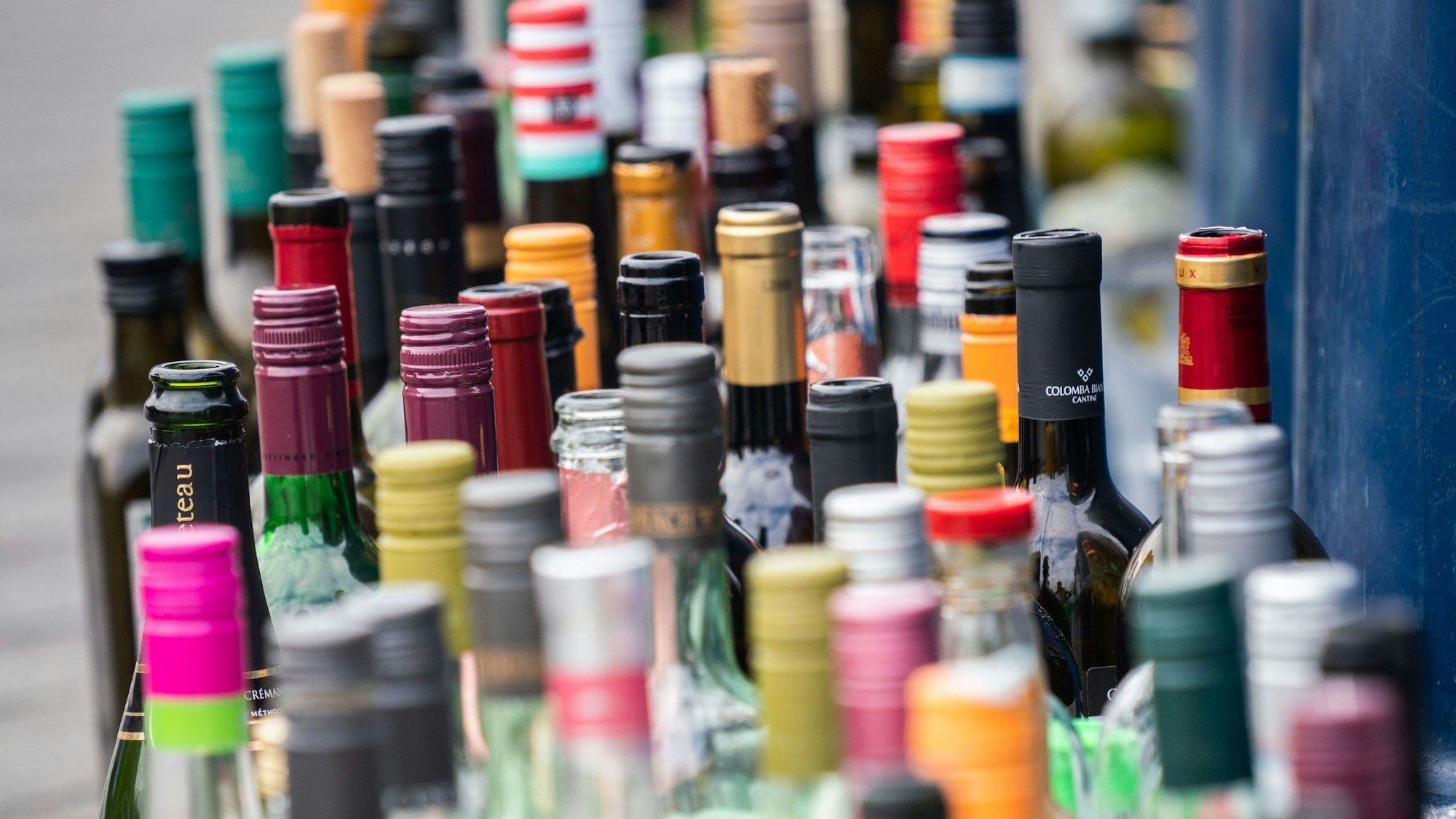 Zahlreiche leere Flaschen stehen vor einem bereits überfüllten Flaschencontainer.