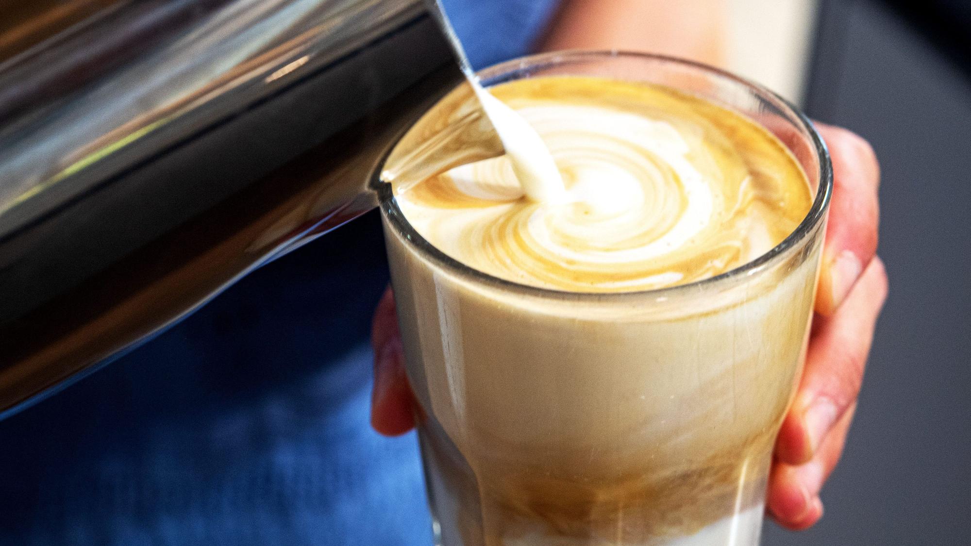 Cremige Milch wird in ein Glas mit Kaffee geschüttet.
