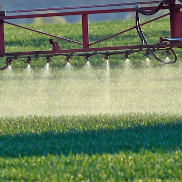 Ein Landwirt fährt mit einer Dünger- und Pestizidspritze über ein Feld mit jungem Getreide.