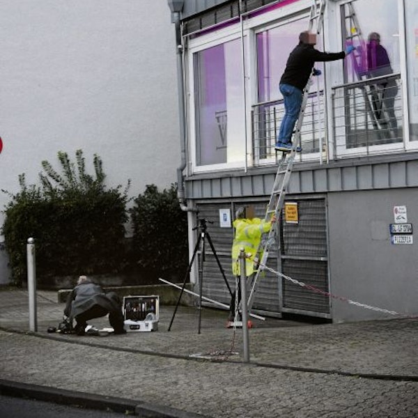Spurensicherer der Polizei stehen auf einer Leider und sichern Spuren an Einschusslöchern in einer Glasfassade.