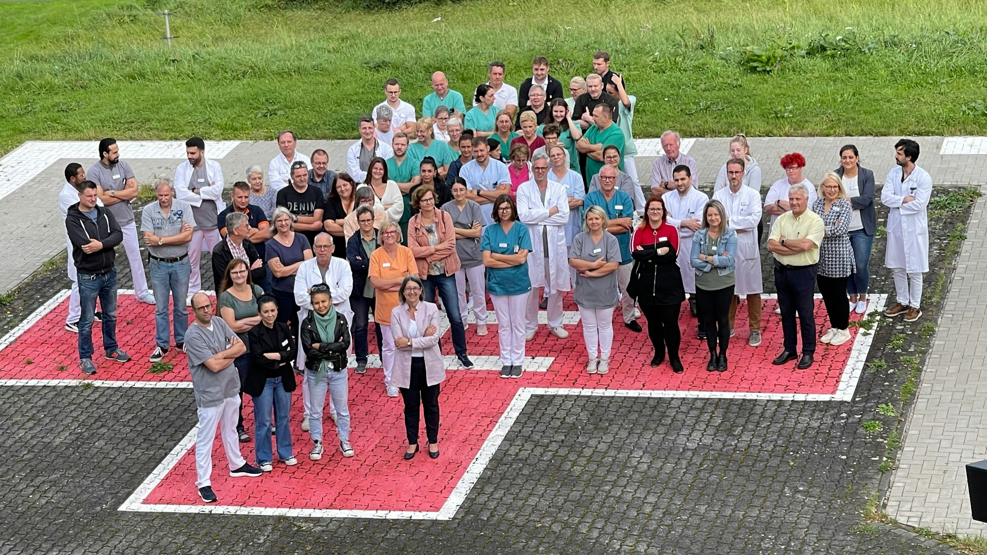 Menschen stehen mit verschränkten Armen auf einem auf das Pflaster aufgemalten roten Kreuz.