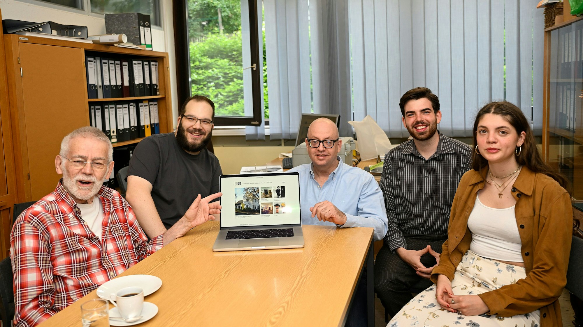 An einem Tisch im Museum sitzt das ehrenamtliche Team des Museums. Auf dem Bildschirm eines Computers ist die neue Homepage zu sehen.