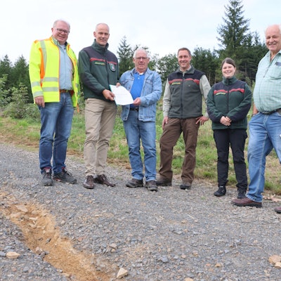 Sechs Personen stehen auf einem geschotterten Waldweg.