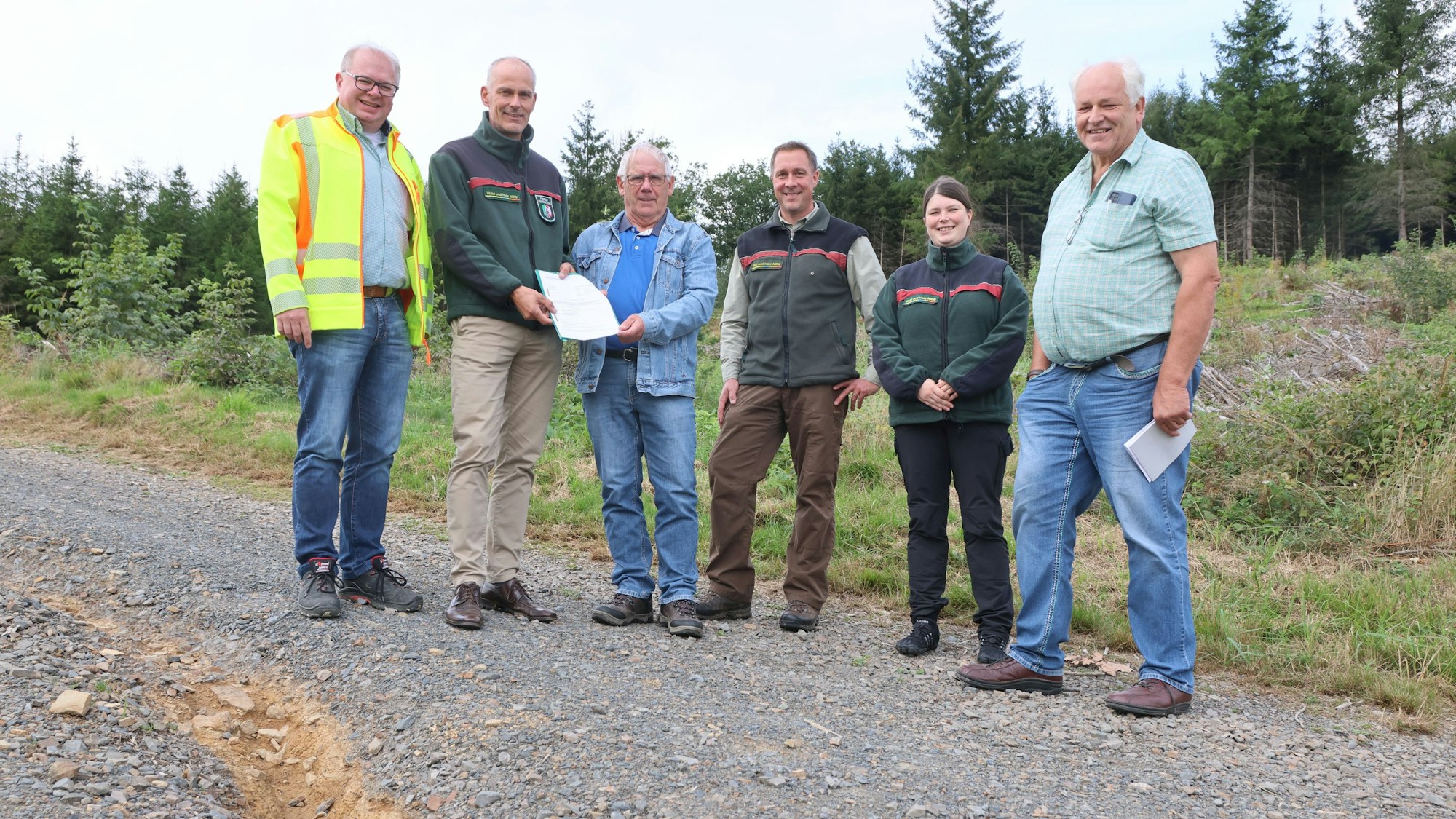 Sechs Personen stehen auf einem geschotterten Waldweg.