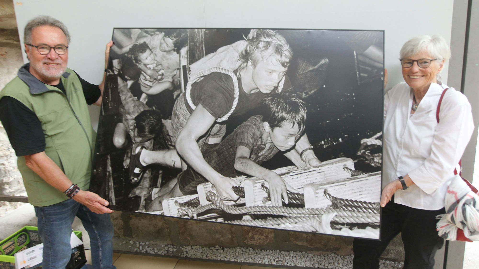 Christel Neudeck und Jürgen Escher halten ein großformatiges Bild. Es zeigt einen vietnamesischen Jungen, der eine Leiter hochklettert.