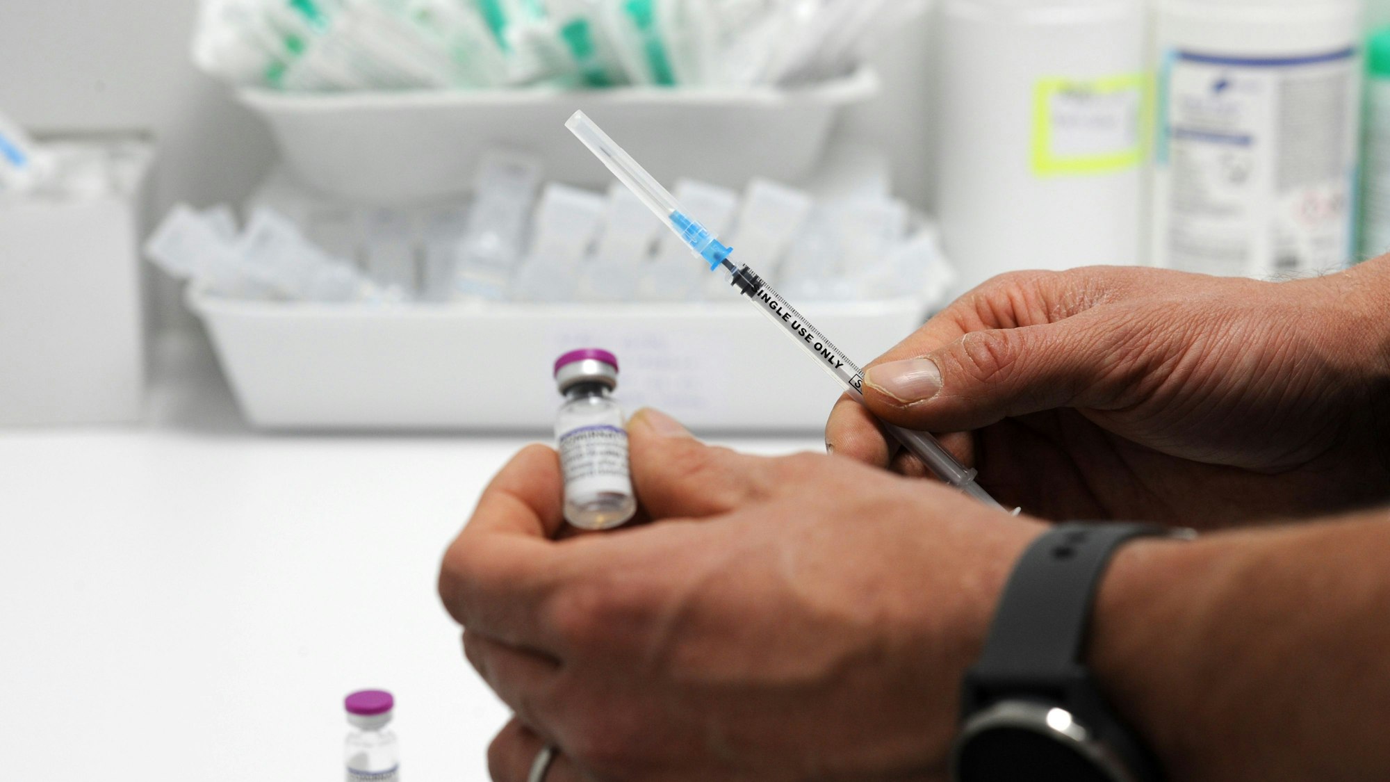 Zwei Hände halten jeweils eine Spritze sowie einen kleinen Glasbehälter mit einem Medikament.