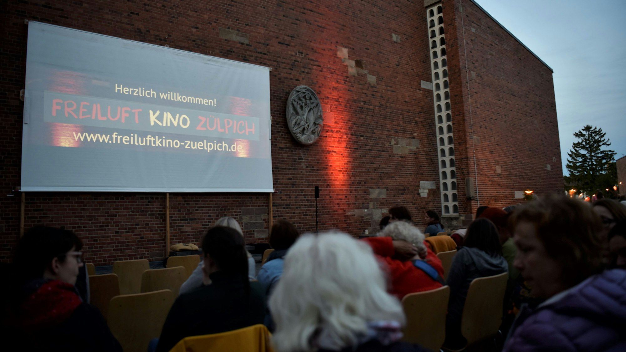Das Foto zeigt die Leinwand auf dem Quiriniusplatz in Zülpich, davor Zuschauer. Das kostenlose Freiluftkino Zülpich findet immer im Frühjahr und im Herbst auf dem Quiriniusplatz statt.