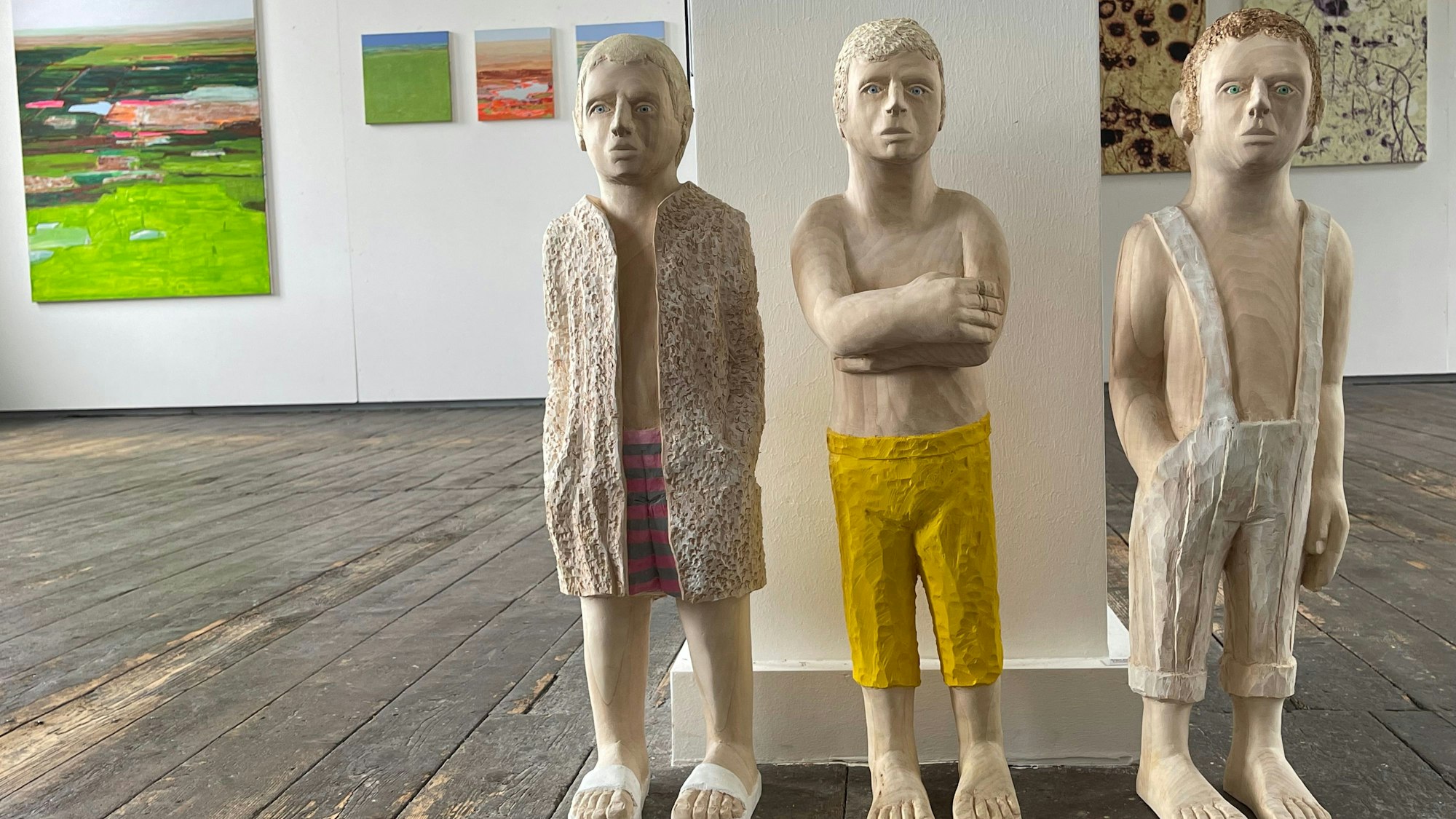 Drei aus Holz geschnitzte Männer stehen nebeneinander, einer hat die Arme verschränkt.
