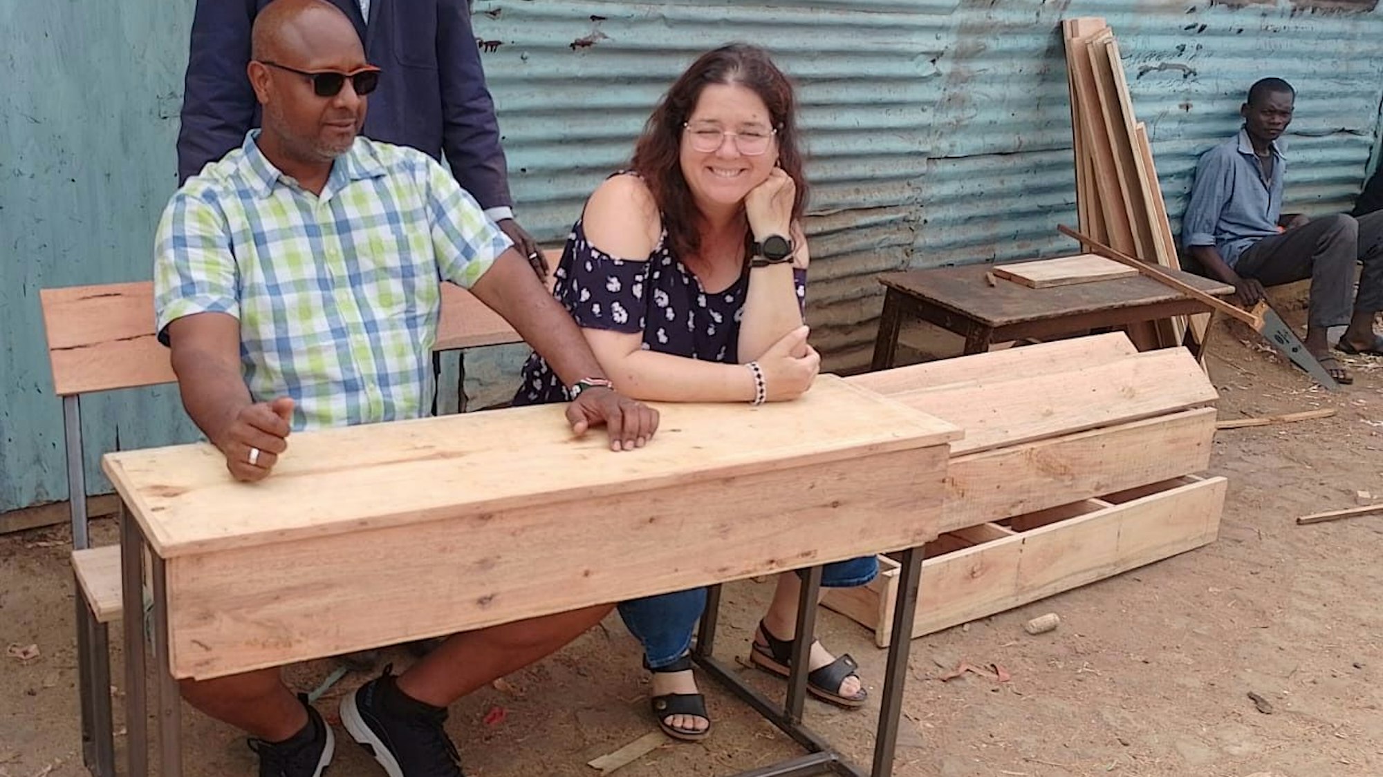 Das Bild zeigt einen Mann und eine Frau, die an einer Schulbank sitzen