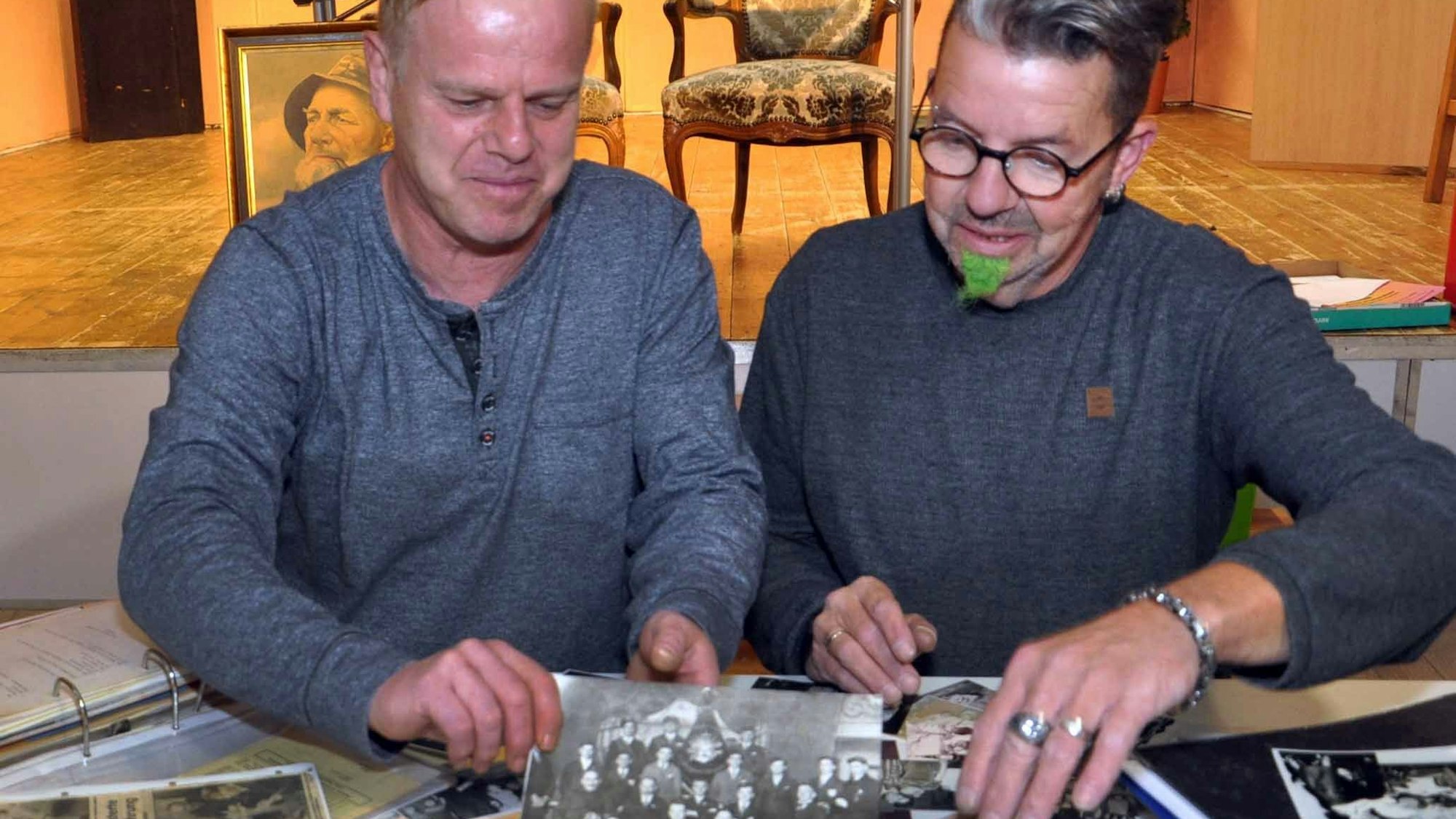 Zwei Männer, Andreas Bellgardt (links) und René Koder, sitzen an einem Tisch und betrachten historische Schwarz-Weiß-Fotos.