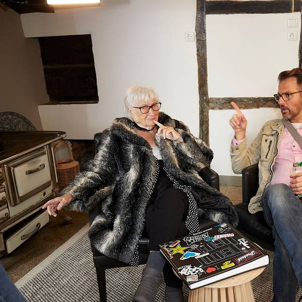 Ingo Wolfgarten und seine Großmutter Liesel Buchheldt sitzen in schwarzen Sesseln und unterhalten sich. Vor ihnen auf dem Tisch liegt ein Fotoalbum.