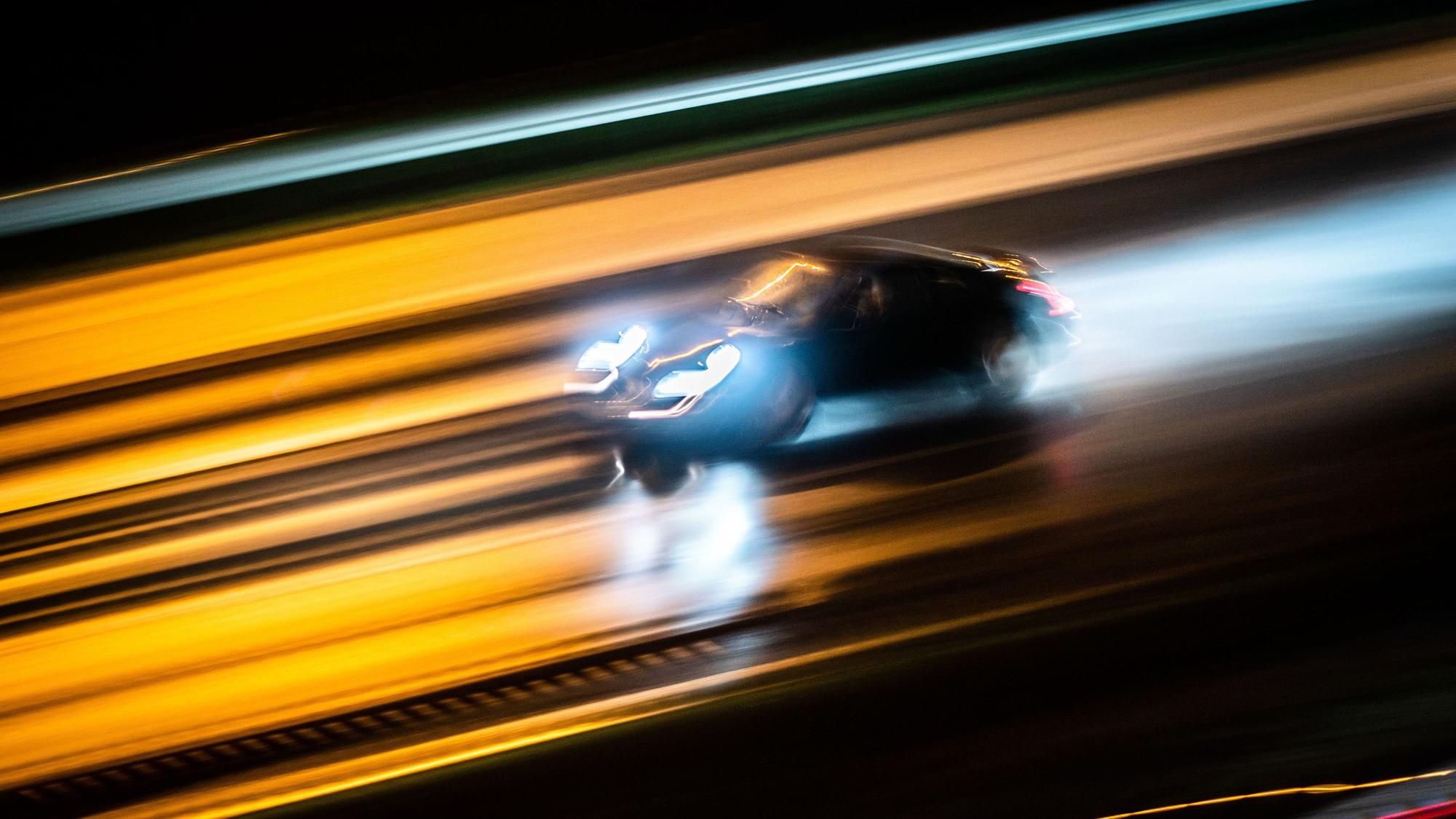 Ein Fahrzeug rast abends über die regennasse Autobahn.