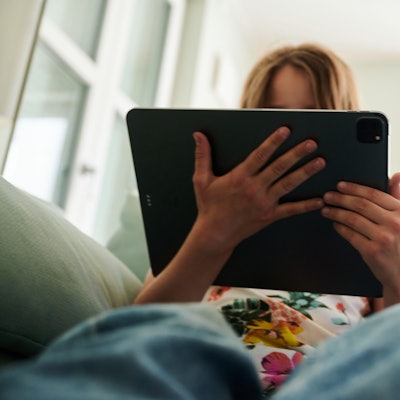 Ein Mädchen sitzt auf der Couch und guckt in das Tablet ihrer Eltern.