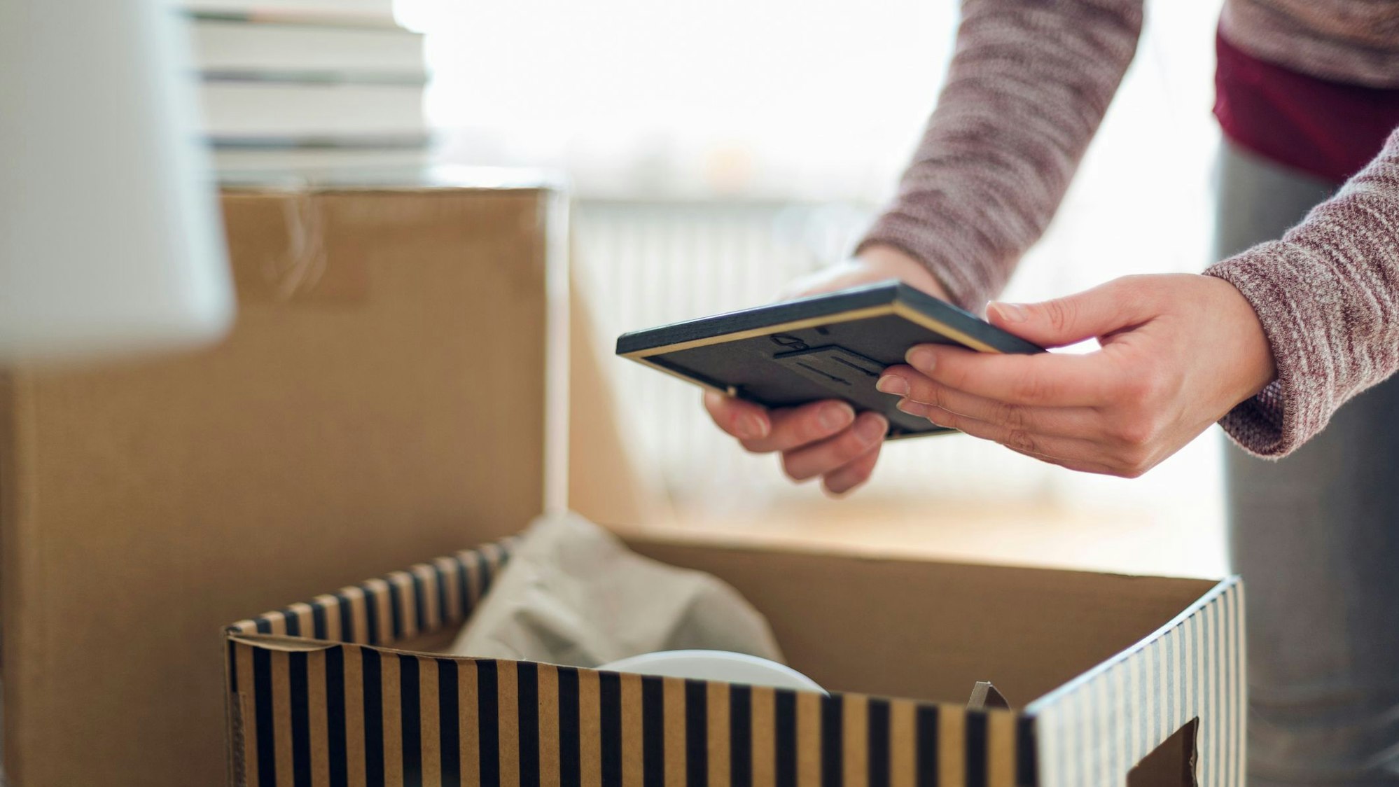 Eine Frau hält vor einem Umzugskarton einen Bilderrahmen in den Händen.