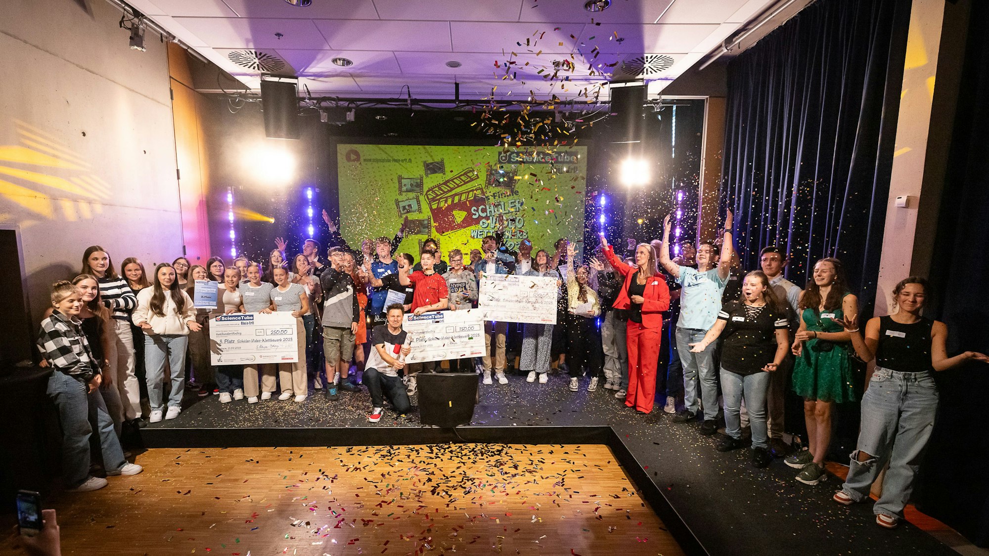 Eine Gruppe von Schülerinnen und Schülern auf einer Bühne im Konfetti-Regen.