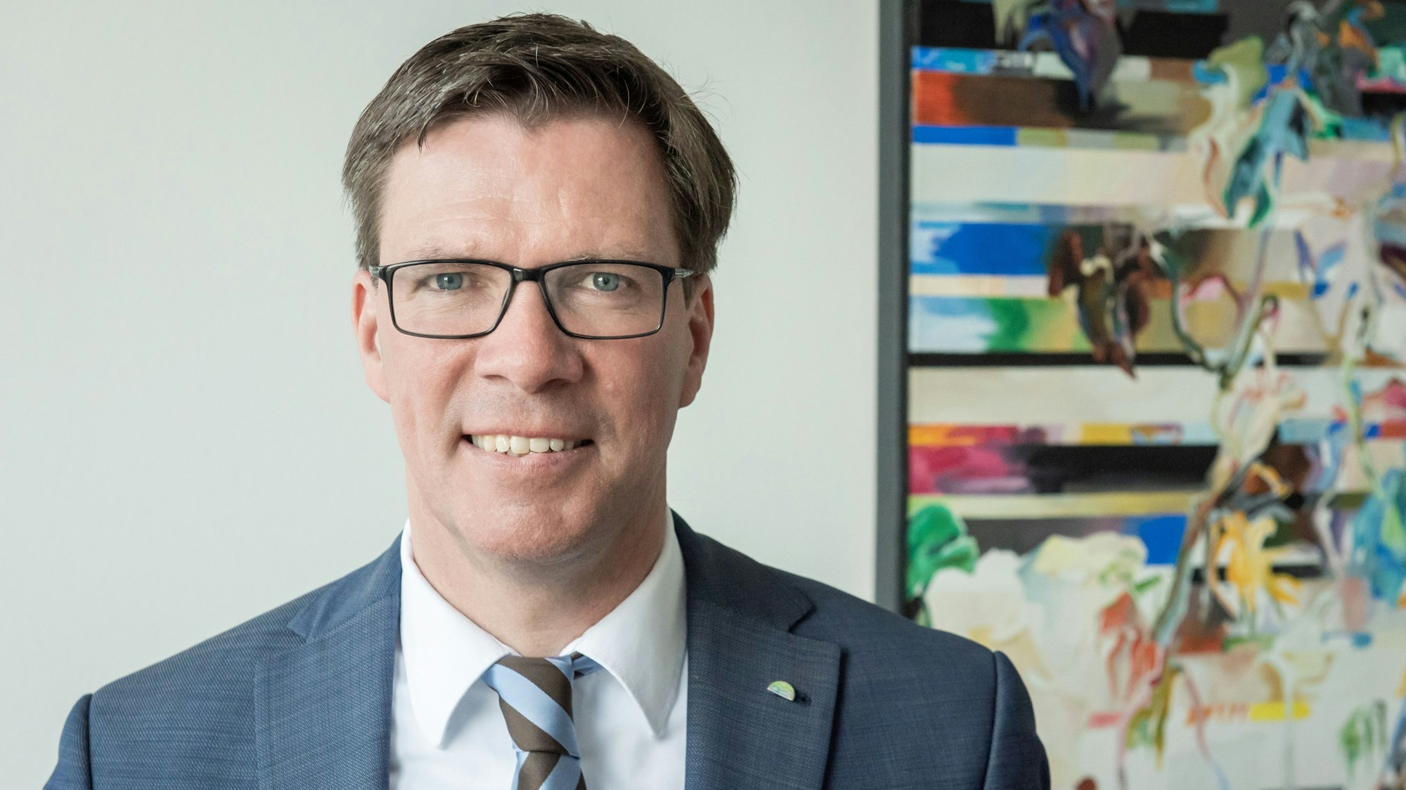 Landrat Stephan Santelmann steht vor einem bunten Bild im Kreishaus.