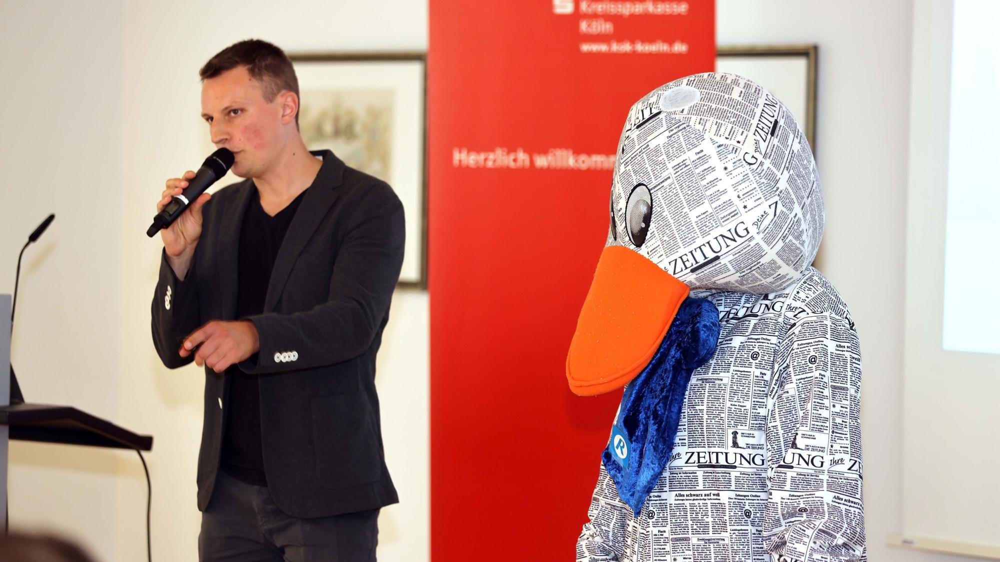 Paula Print steht neben einem Mann, der ein Mikrofon in der Hand hält.