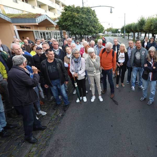 Eine Gruppe von Menschen steht auf der Rheinallee und der Stadtbahntrasse in der Altstadt von Königswinter.