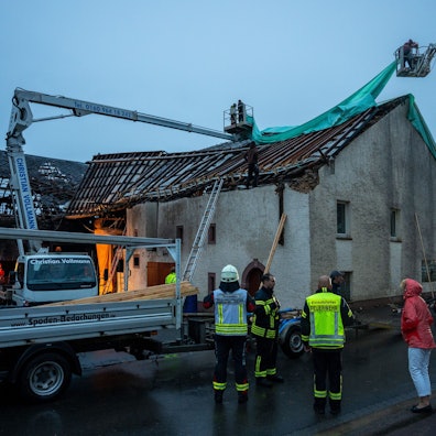 Feuerwehr und Einsatzkräfte kämpfen mit Schäden an einem abgedeckten Häuserdach im rheinland-pfälzischen Nusbaum, die durch einen Tornado verursacht wurden.