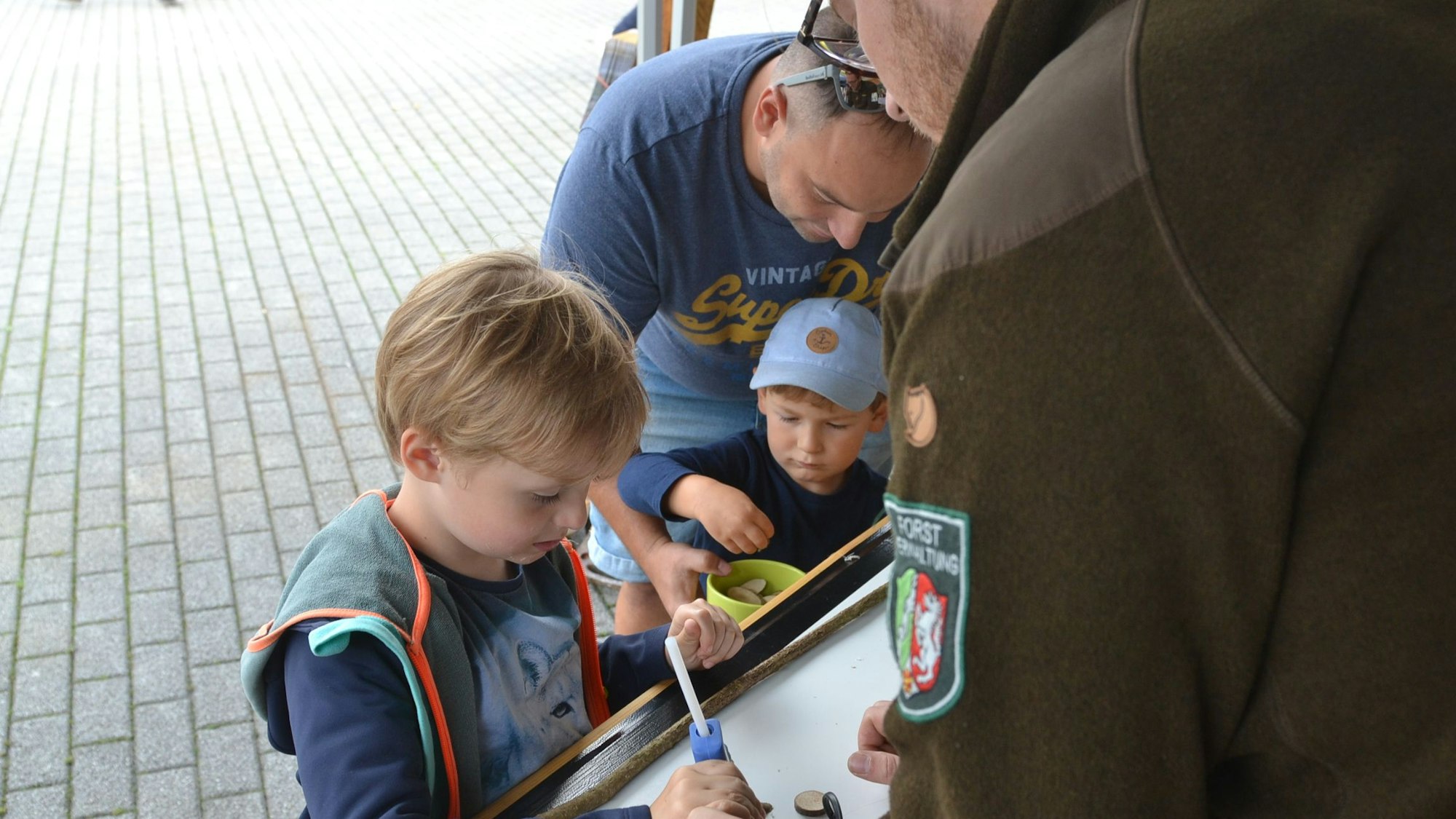 Kinder stehen an einem Stand und spielen mit Holz.
