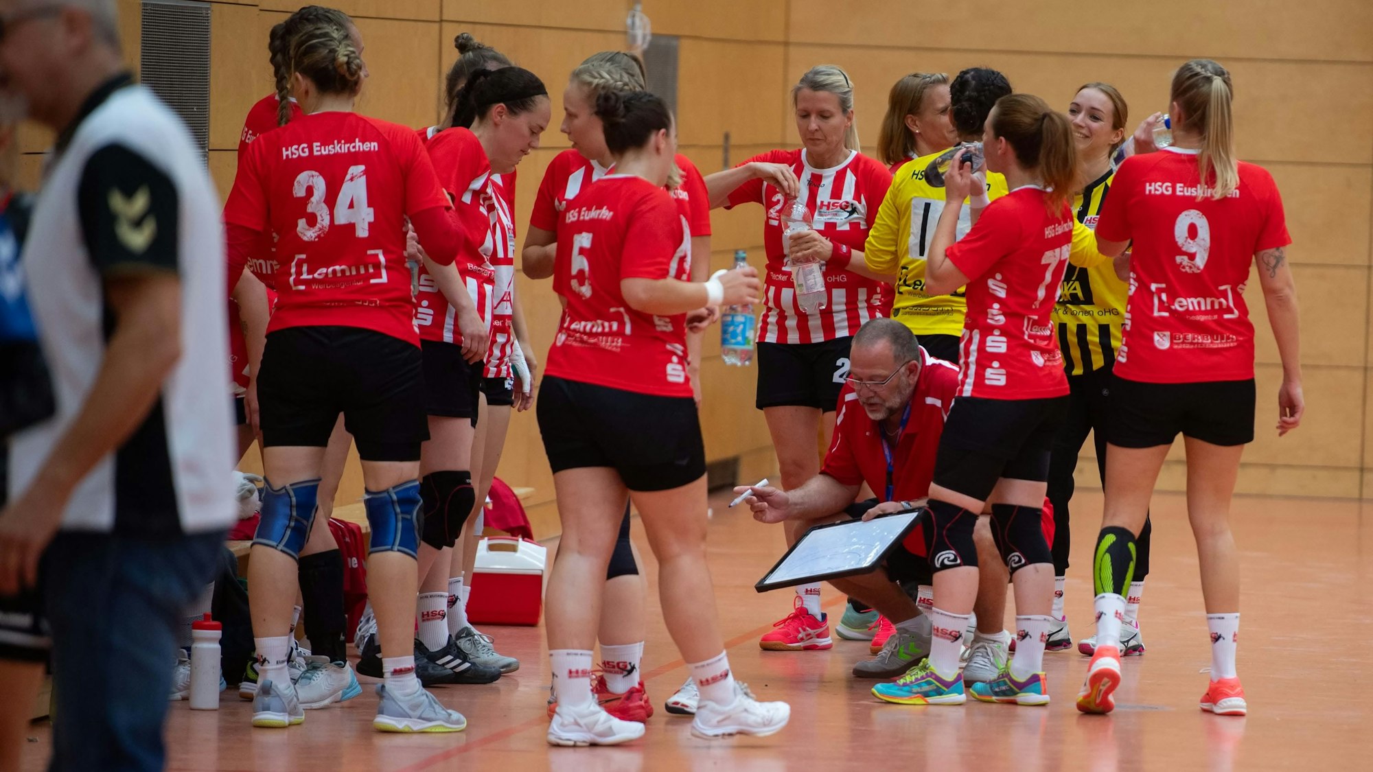 Die Spielerinnen stehen um ihren Trainer herum, der auf dem Boden hockt und eine Taktiktafel zeigt.