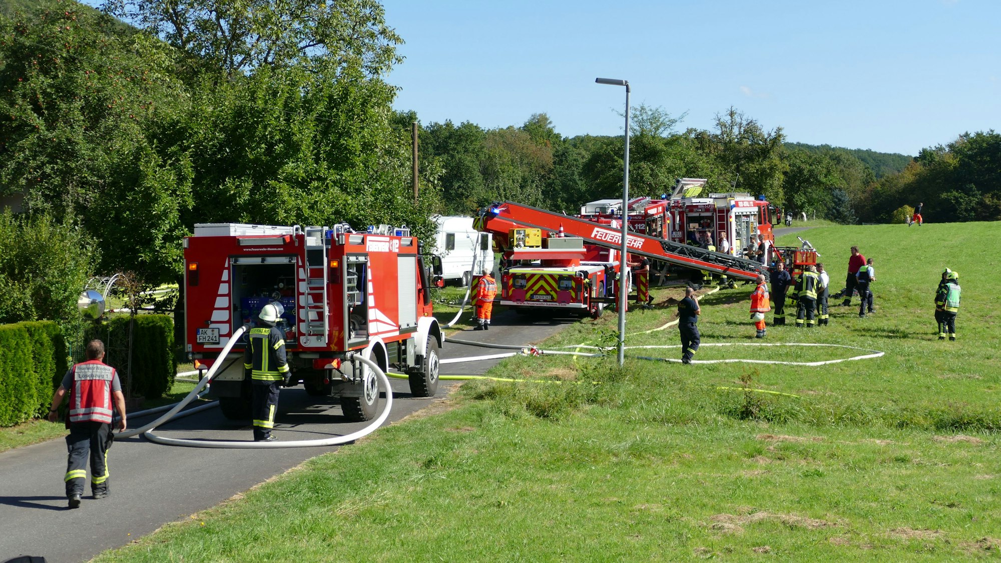 Auf einer Straße und der angrenzenden Wiese stehen mehrere Löschfahrzeuge der Feuerwehr.