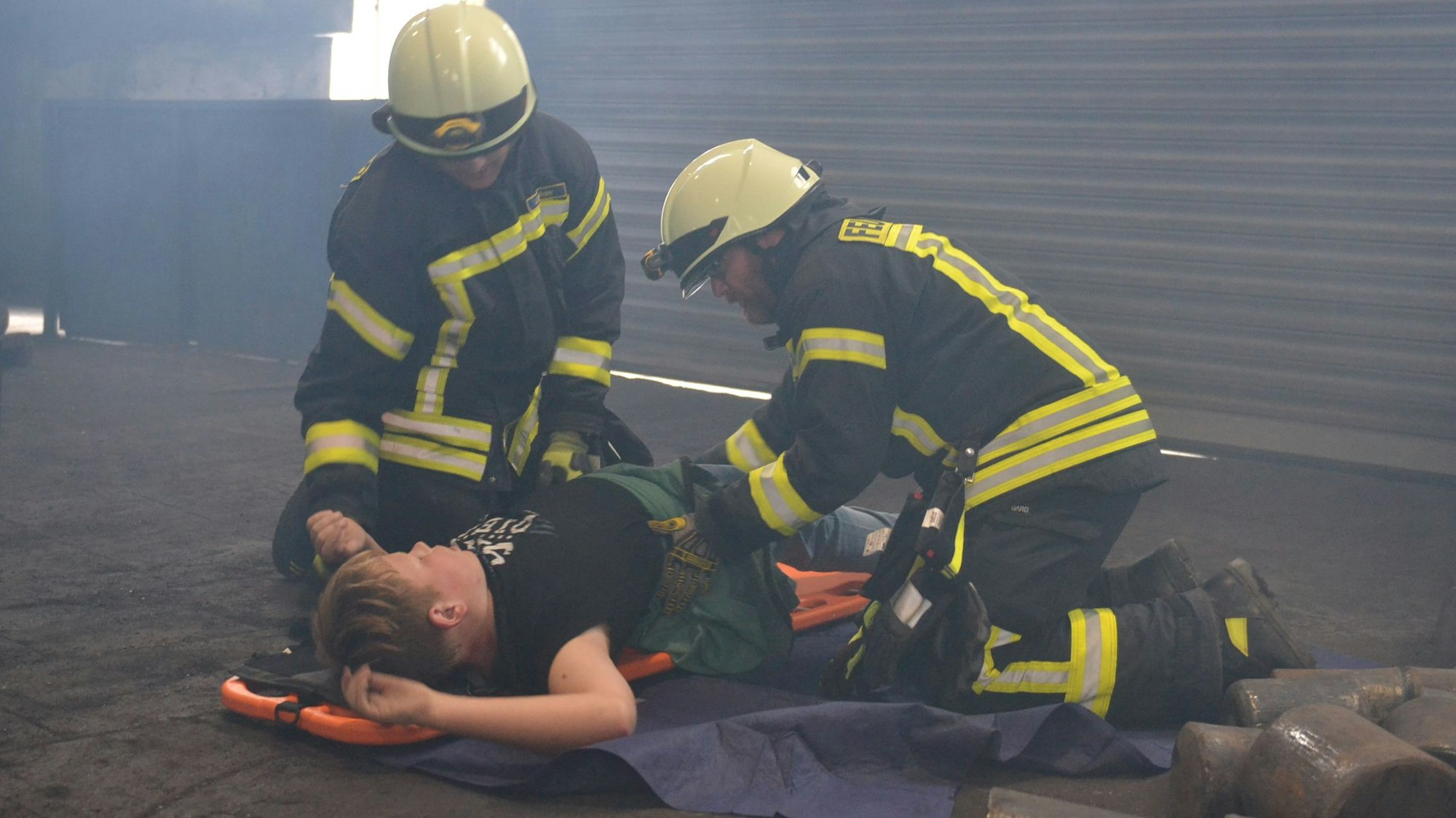 Das Bild zeigt zwei Feuerwehrmänner, wie sie einen Darsteller versorgen.