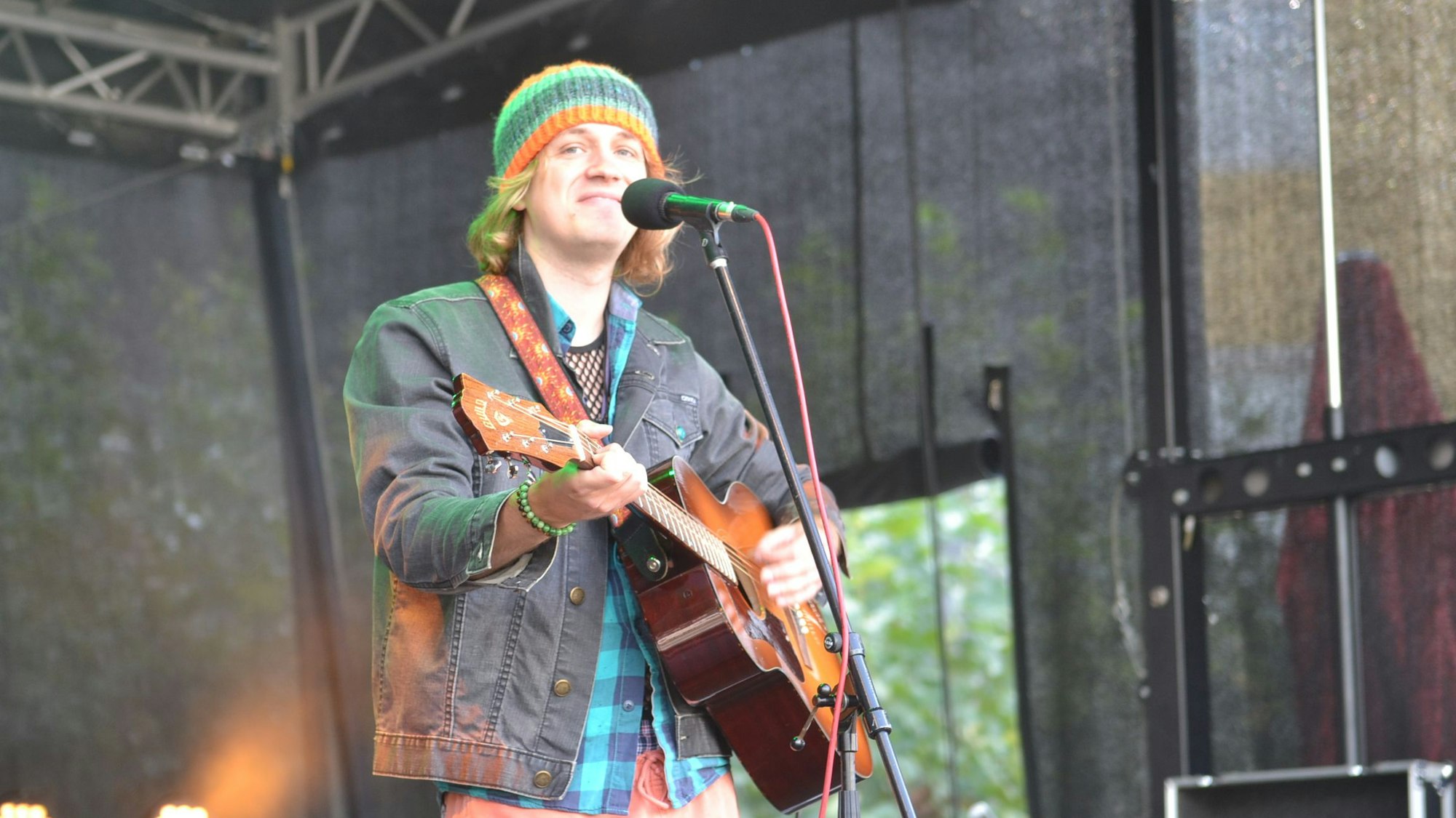Ein junger Musiker steht mit seiner Gitarre auf der Bühne.