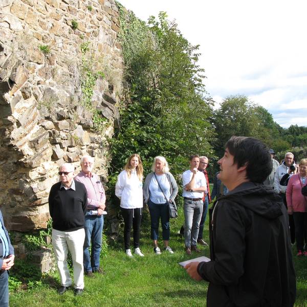 Eine Gruppe von Menschen steht mit dem Bürgermeister an der mittelalterlichen Stadtmauer von Stadt Blankenberg.