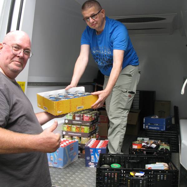 Ein Mann reicht einem anderen Mann, der in einem Transporter steht einen Karton mit gespendeten Lebensmitteln an.