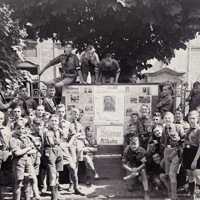 Jungen in HJ-Uniformen stehen vor einem großen Schaukasten.