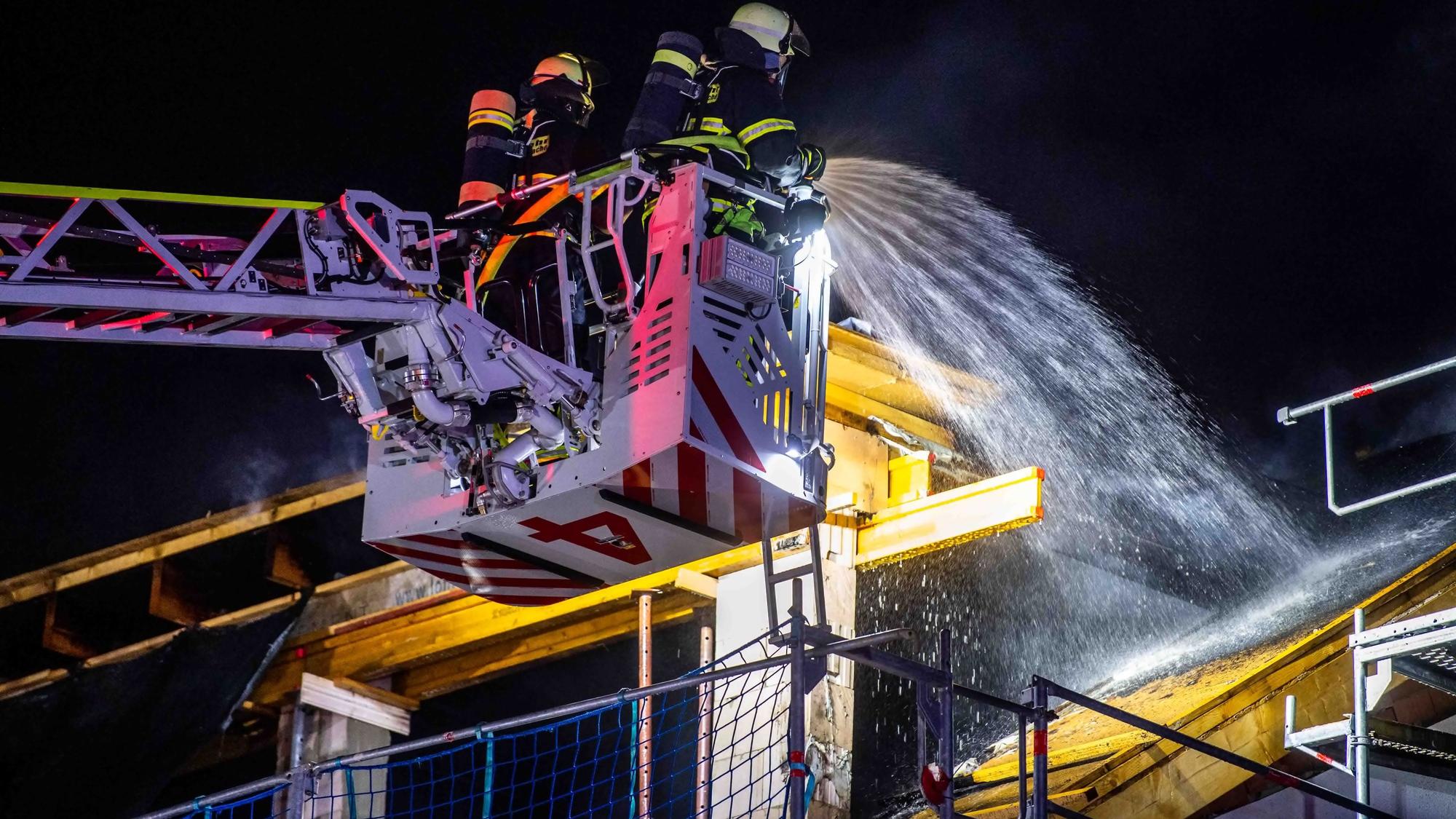 Das Bild zeigt zwei Feuerwehrleute, die den Brand von der Drehleiter aus bekämpfen.