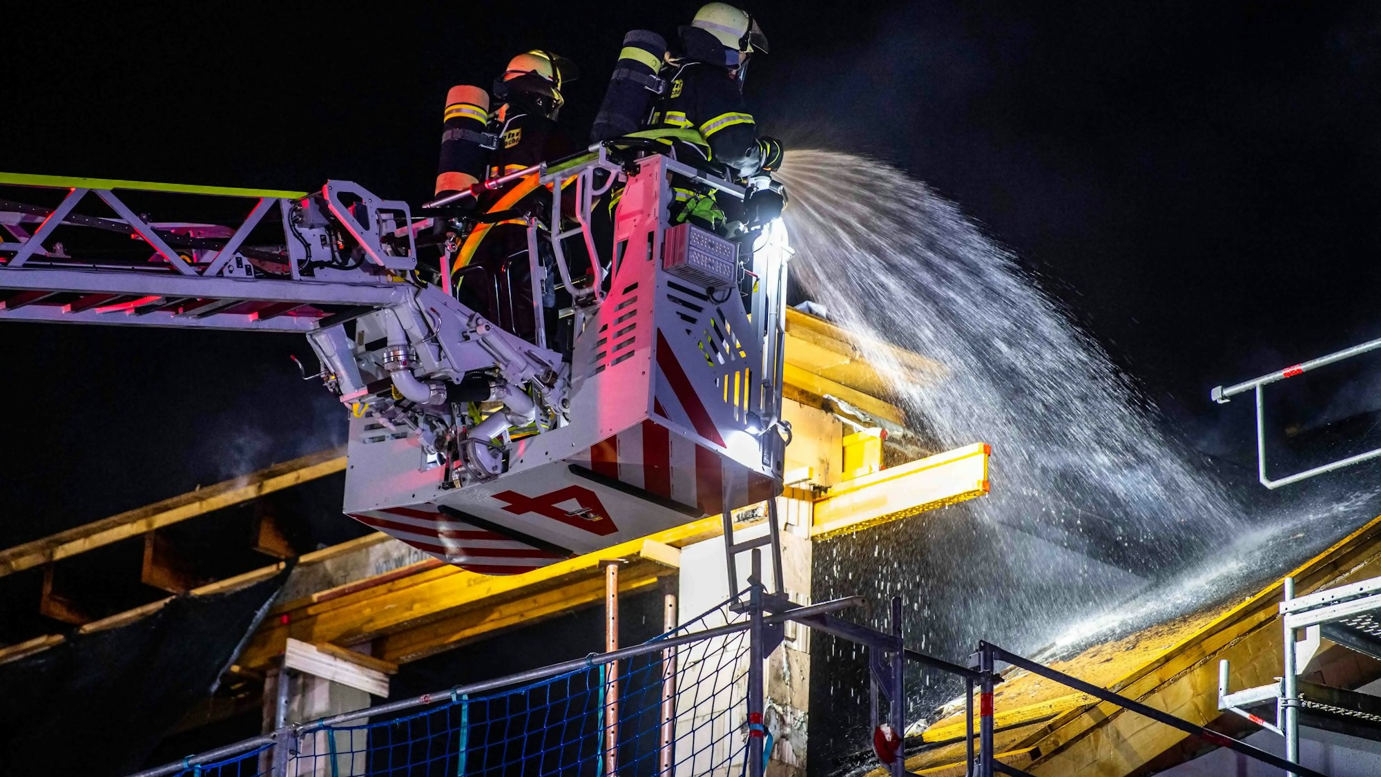 Das Bild zeigt zwei Feuerwehrleute, die den Brand von der Drehleiter aus bekämpfen.