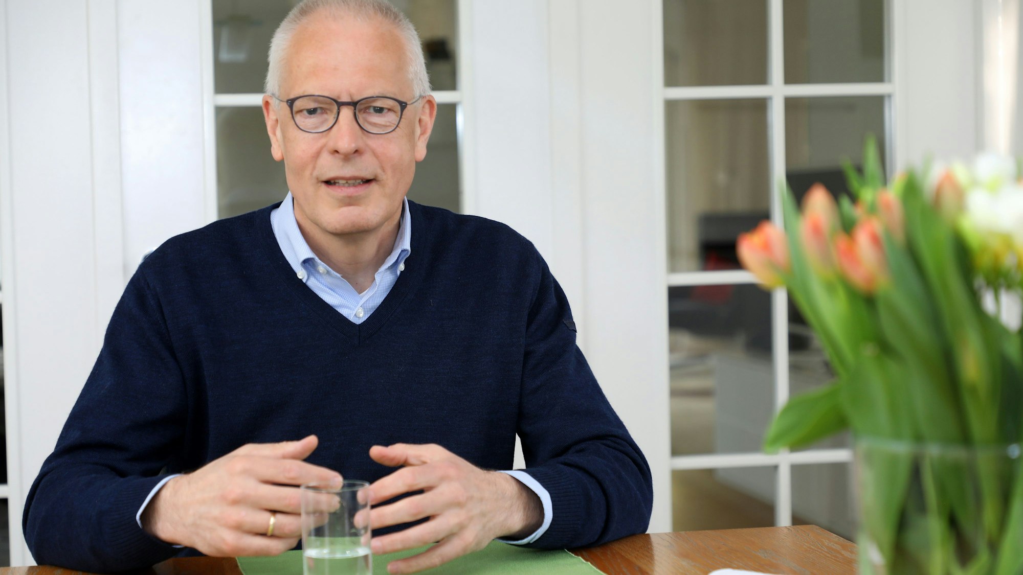 MdB Dr. Hermann-Josef Tebroke sitzt an einem Tisch mit Tulpen an seiner Wohnadresse in Lindlar in einem Interview.