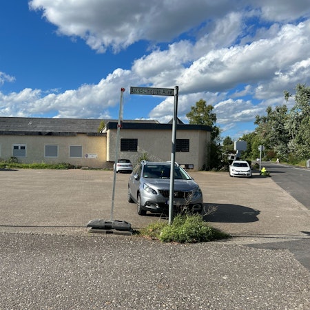 Ein fast leerer Parkplatz vor einem einstöckigen Gebäude ist zu sehen.