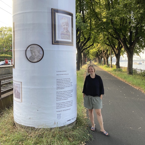 Eine Frau mit blondem Pagenkopf steht neben einer Litfaßsäule, die mit Texten und Bildern beklebt ist.