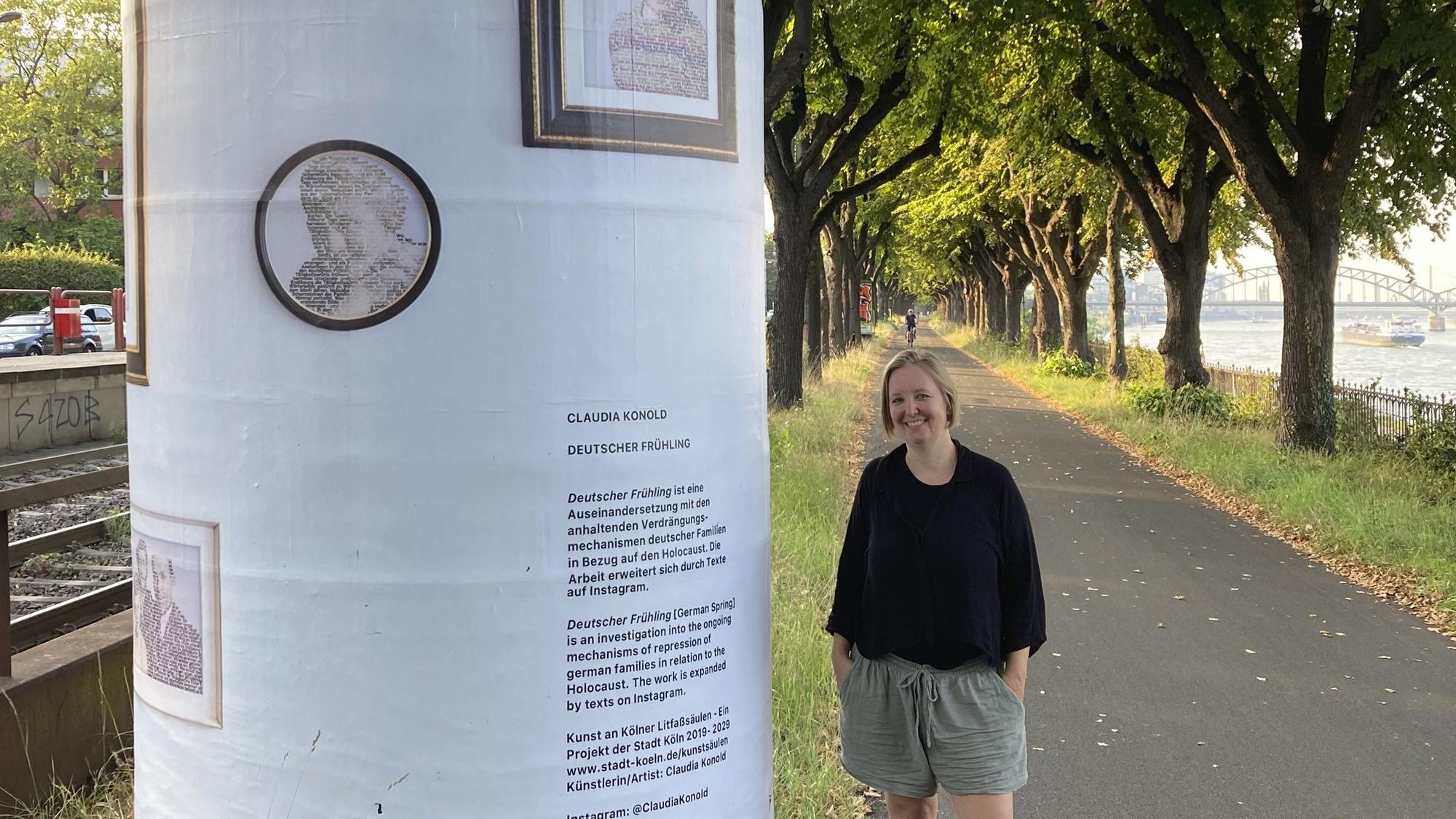 Eine Frau mit blondem Pagenkopf steht neben einer Litfaßsäule, die mit Texten und Bildern beklebt ist.