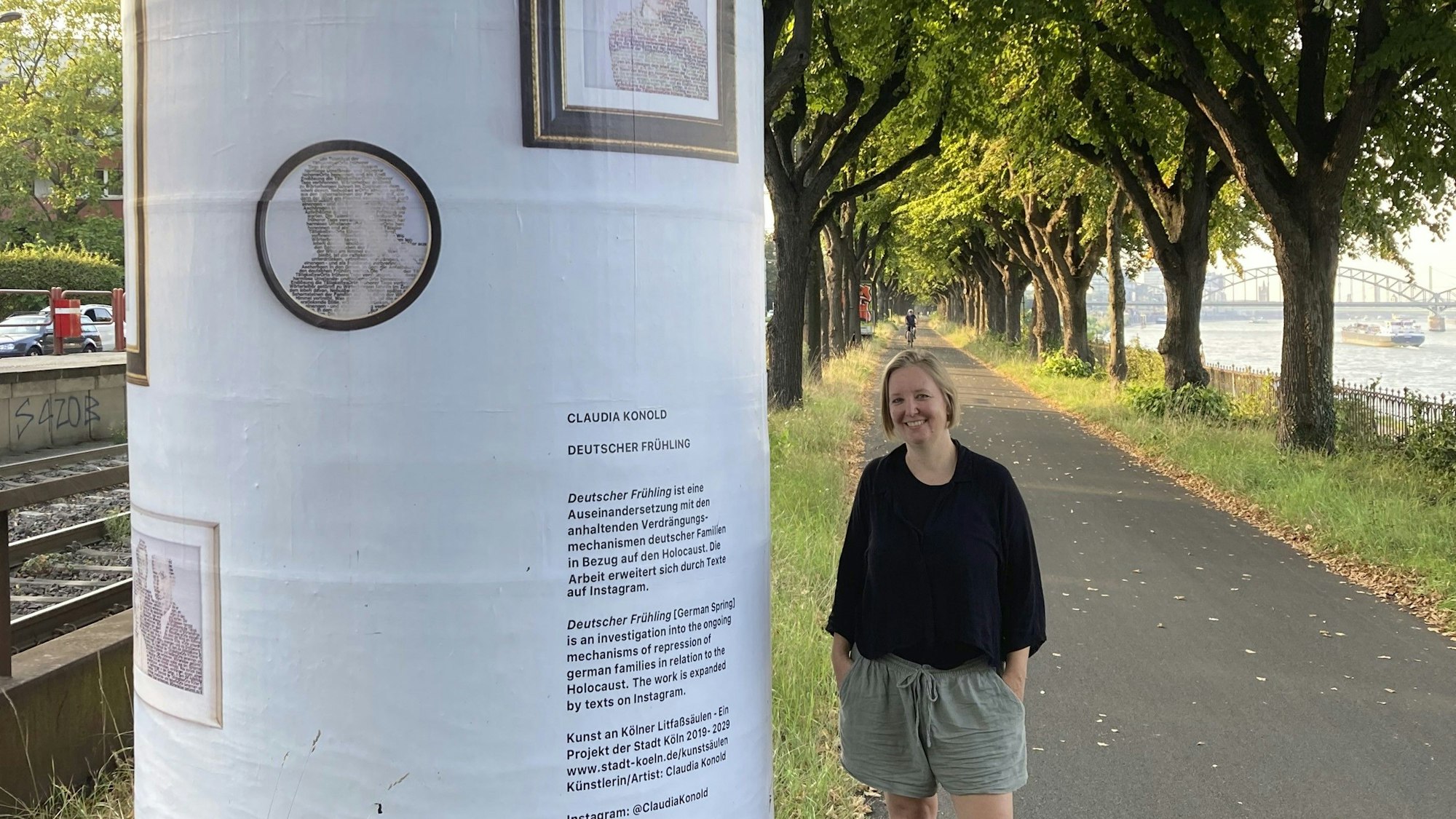 Eine Frau mit blondem Pagenkopf steht neben einer Litfaßsäule, die mit Texten und Bildern beklebt ist.