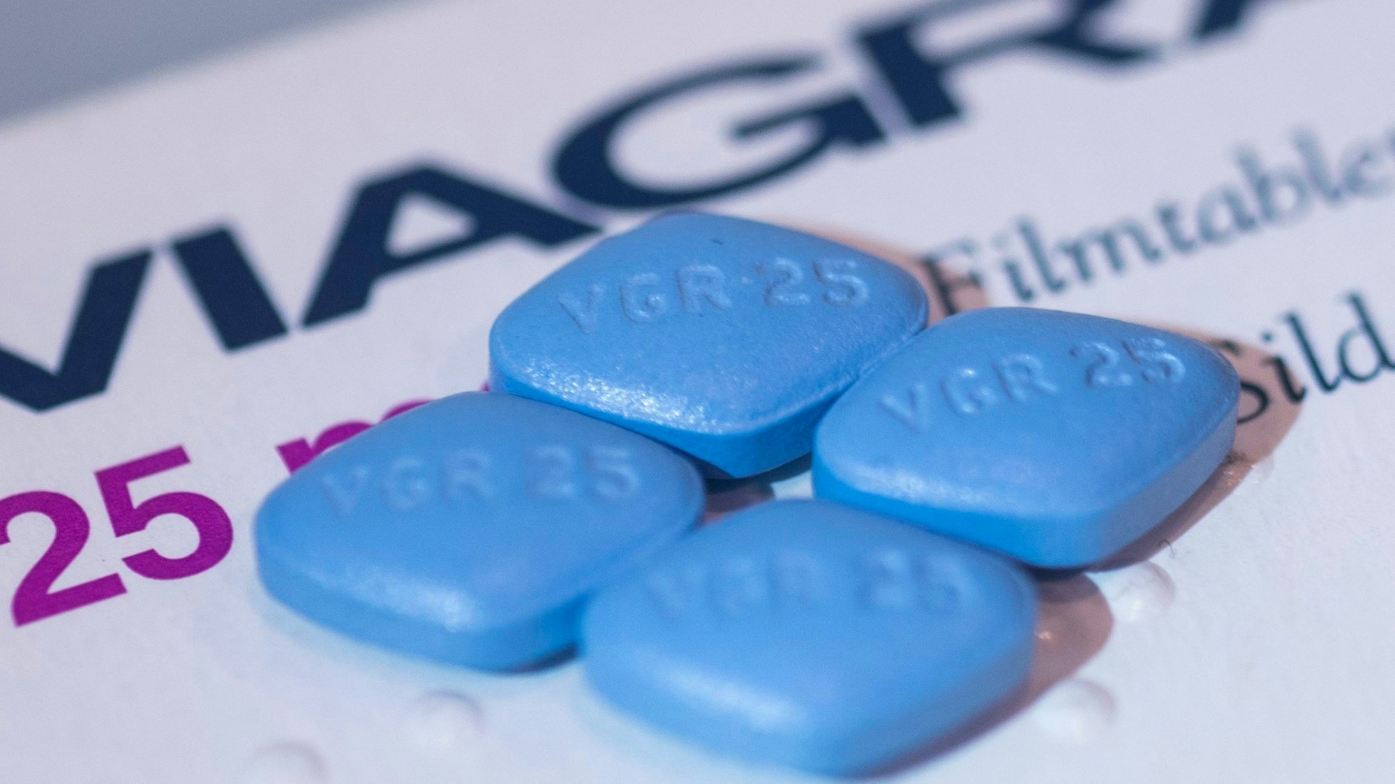 Vier Viagra-Tabletten liegen auf einer Viagra-Packung.
