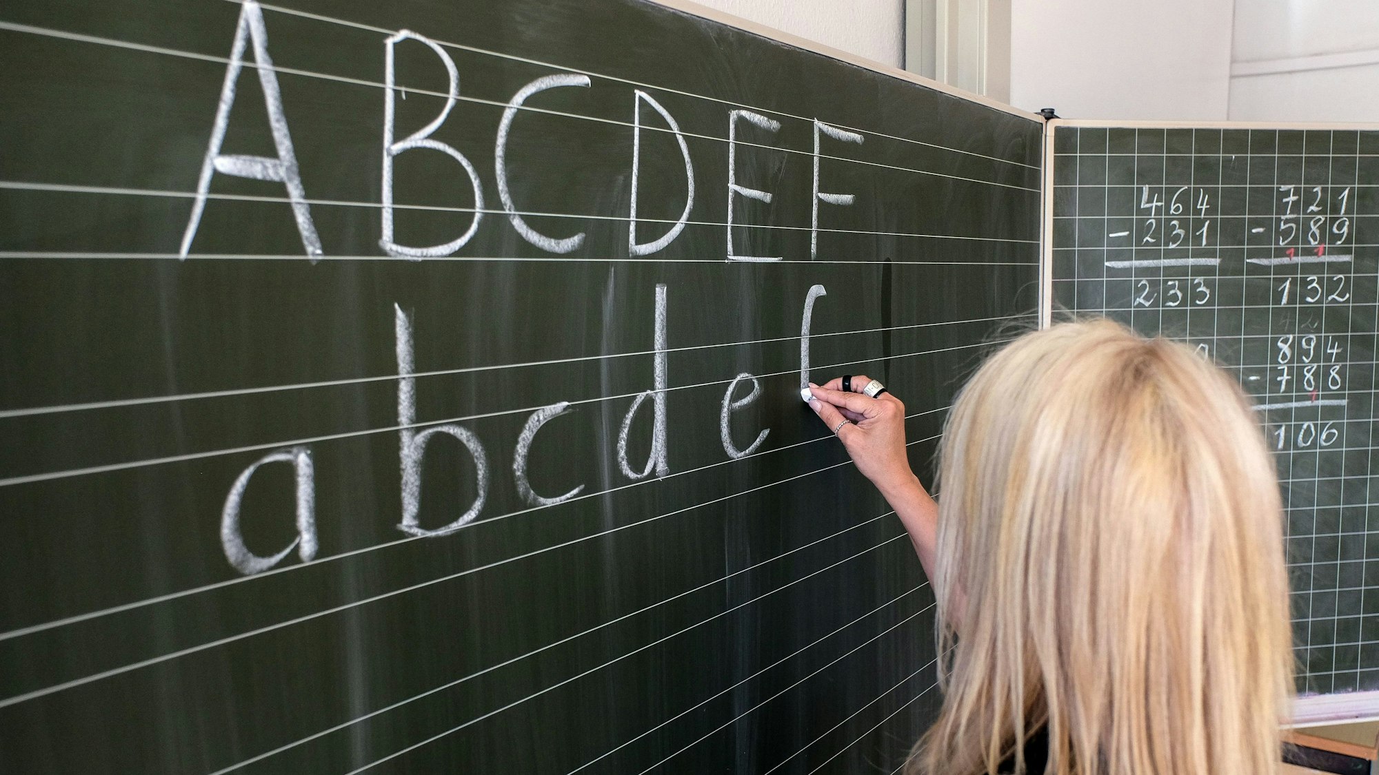 Eine Lehrerin malt das ABC an eine Tafel.