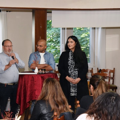 Mehrere Menschen verschiedener Kulturen stehen an einem Tisch bei einem Gespräch zusammen.
