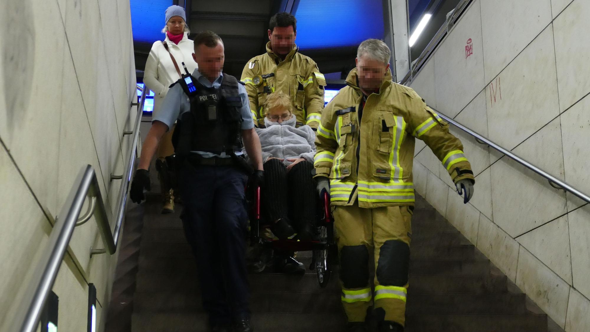 Feuerwehrleute tragen eine Frau im Rollstuhl eine Treppe herunter.
