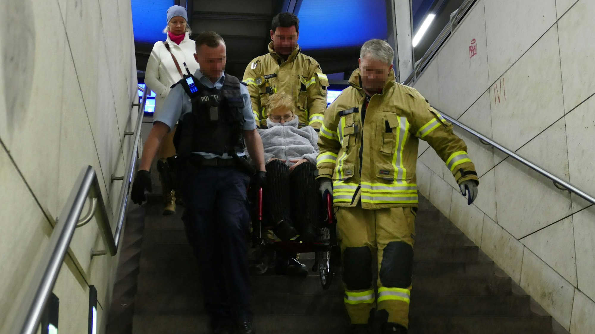 Feuerwehrleute tragen eine Frau im Rollstuhl eine Treppe herunter.